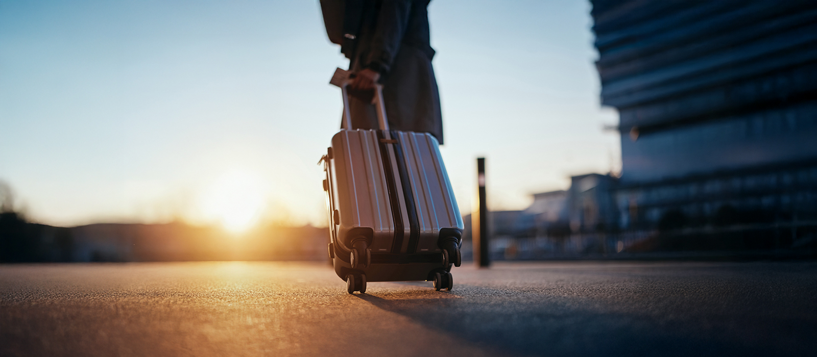 A woman pulling her luggage along the road during sunset.