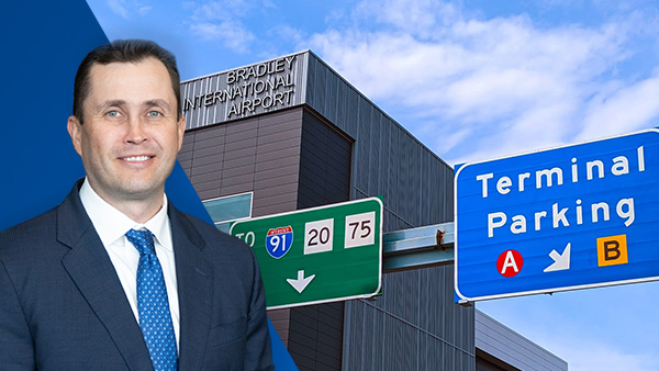 Michael Shea stands in front of Bradley International Airport, with terminal parking and highway directional signs visible in the background.