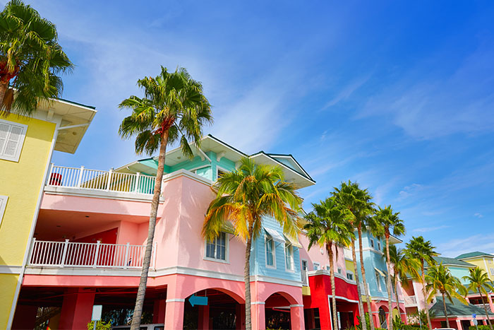 Colorful pastel-hued waterfront buildings with balconies stand behind swaying palm trees in Fort Myers.