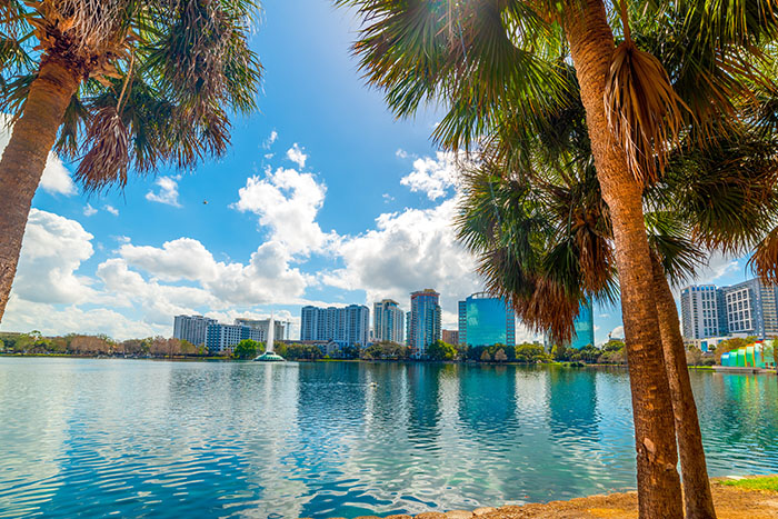 Palm trees frame a downtown Orlando skyline reflected in the calm waters of a city lake.